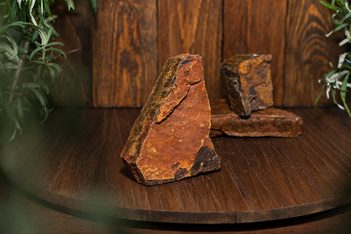 Three rough, brownish-orange mineral specimens with dark edges rest on a dark wooden surface against a wood-paneled background.