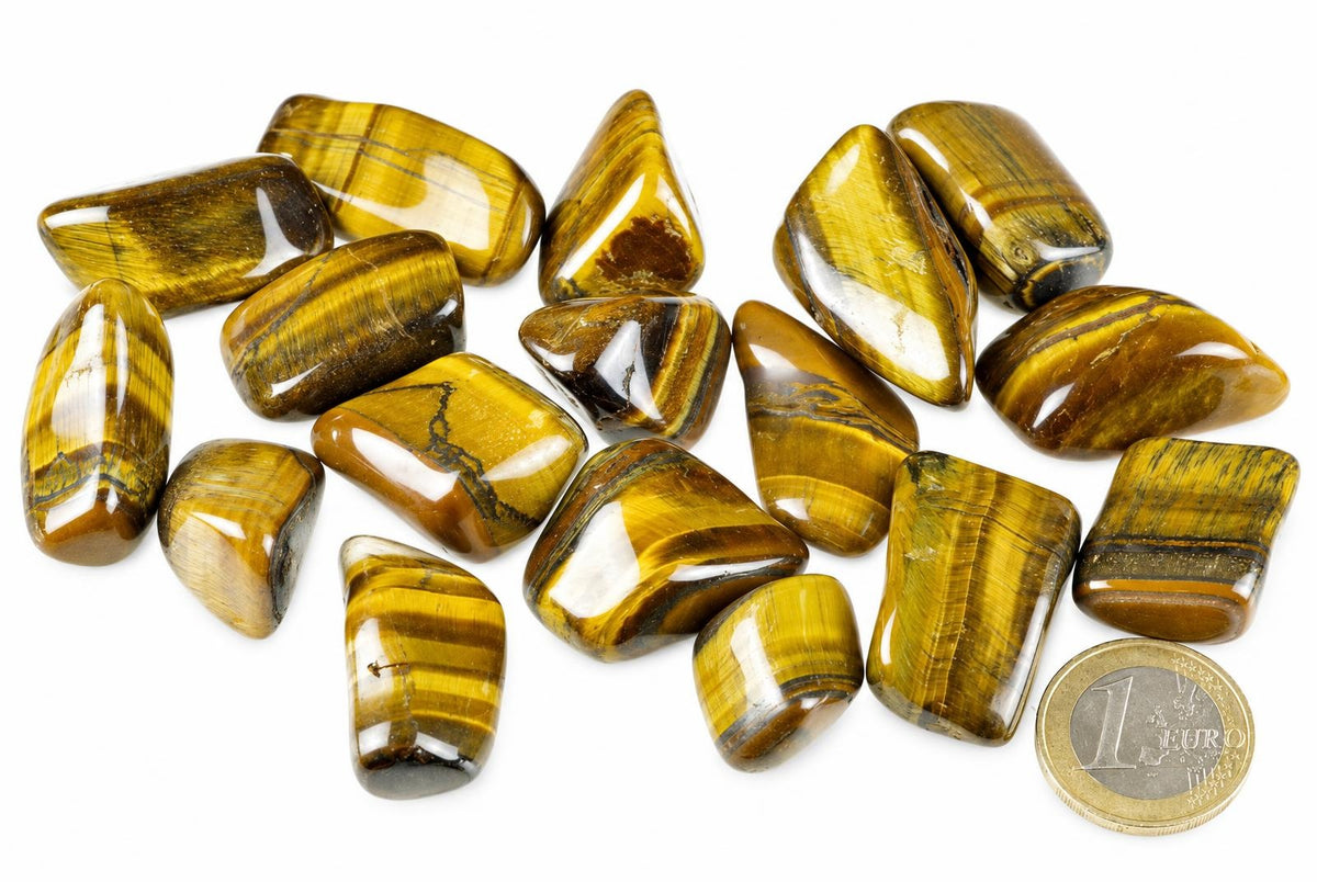 Polished natural Tiger eye tumbled stones with golden brown and yellow striped patterns arranged next to a one euro coin for size comparison.