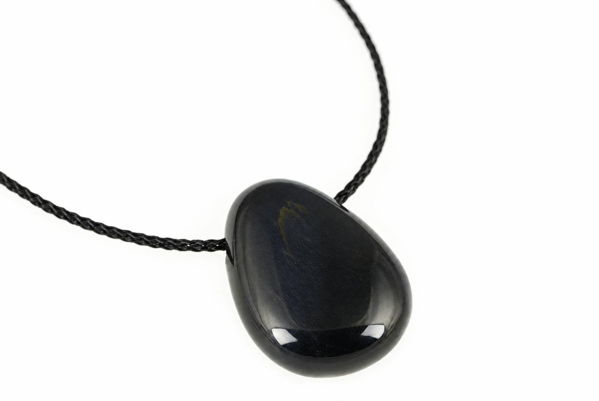 A polished, teardrop-shaped pendant with a dark blue surface and subtle golden streaks hangs from a black cord against a white background.