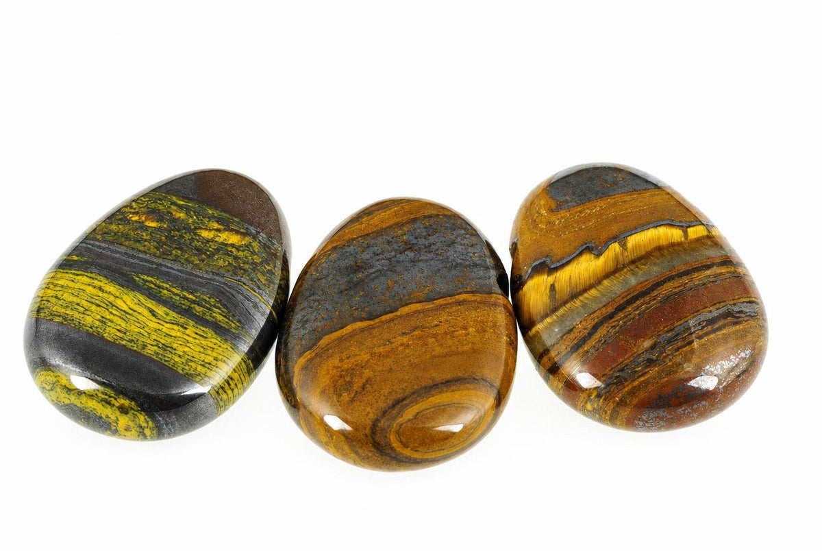 Three polished tiger eye stones with yellow, brown and dark stripes arranged on a white surface.