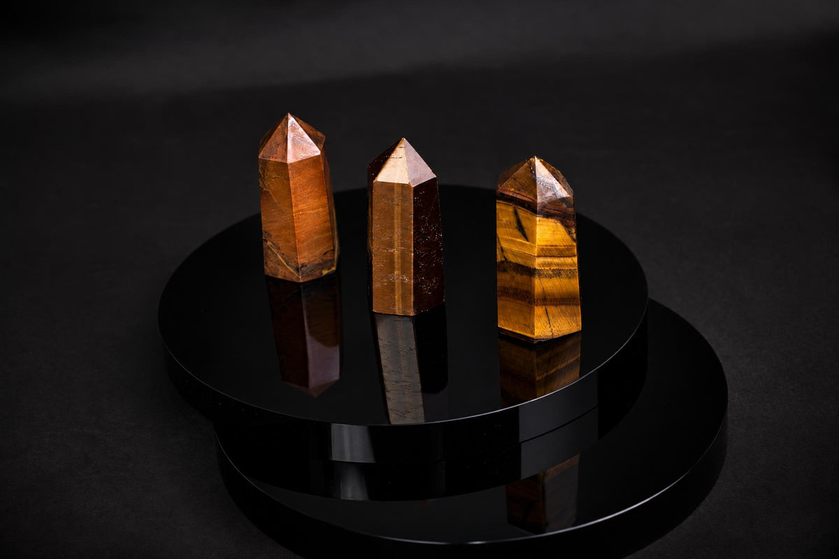Three polished tiger eye obelisks with golden-brown stripes stand on a glossy black circular base against a dark background.