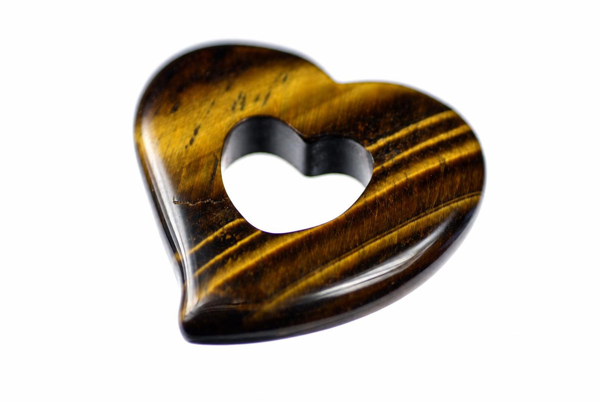 A polished tiger eye heart pendant with a heart shaped cutout and golden brown bands rests on a white background.
