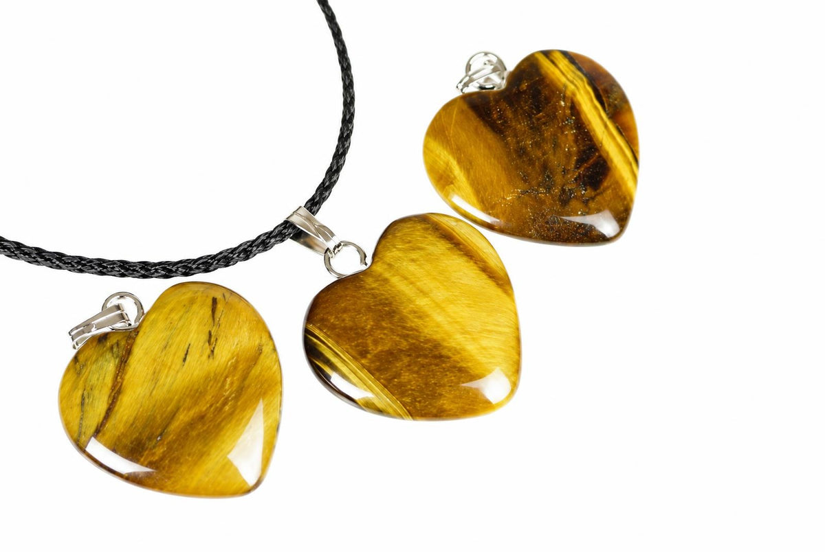 Three polished heart-shaped tiger eye pendants with silver-toned findings on a dark braided cord, set against a white background.