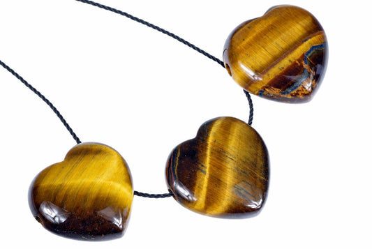 Three heart-shaped tiger eye beads on a dark cord against a white background.