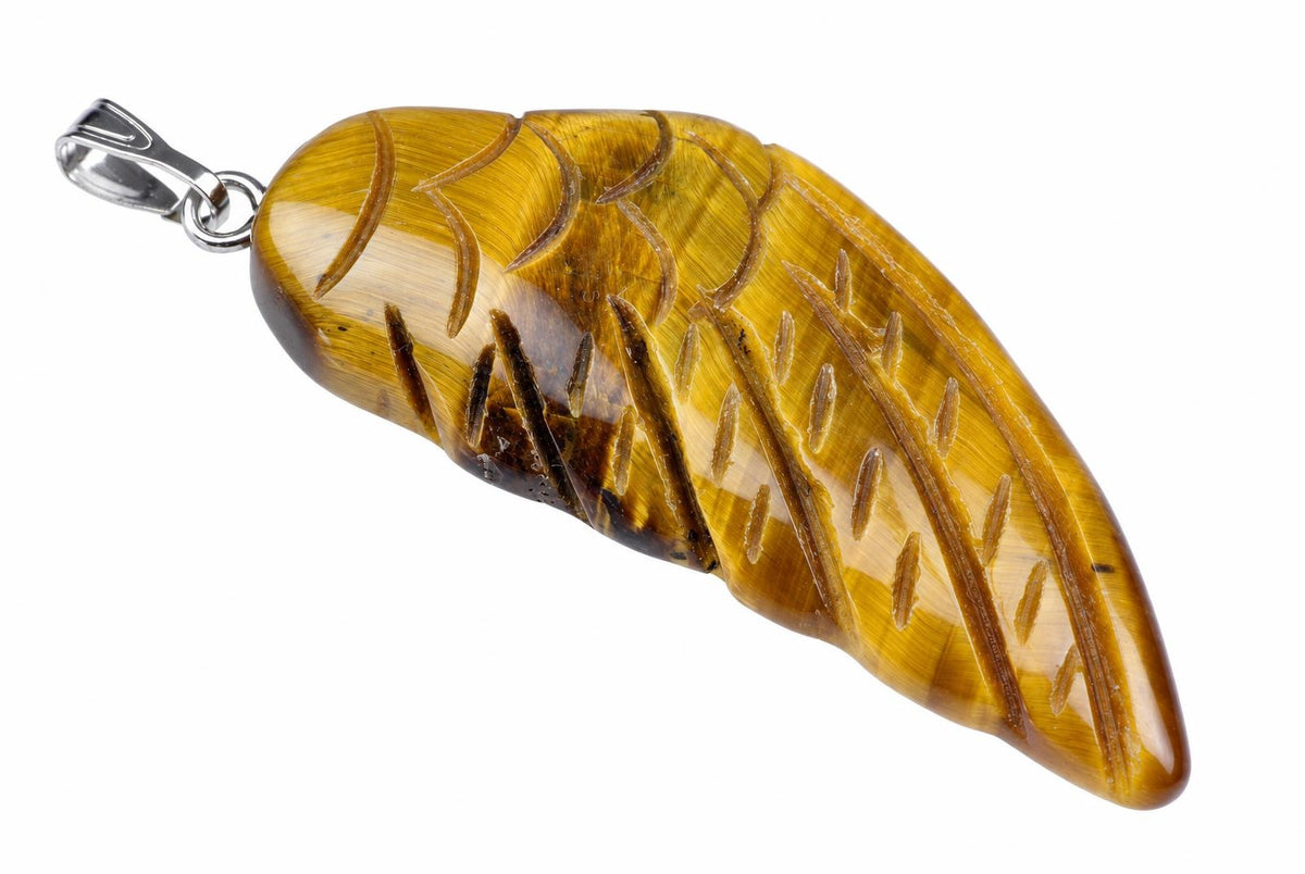 A polished yellow-brown pendant shaped like a wing, with carved lines and dark inclusions, attached to a silver-toned bail on a white surface.