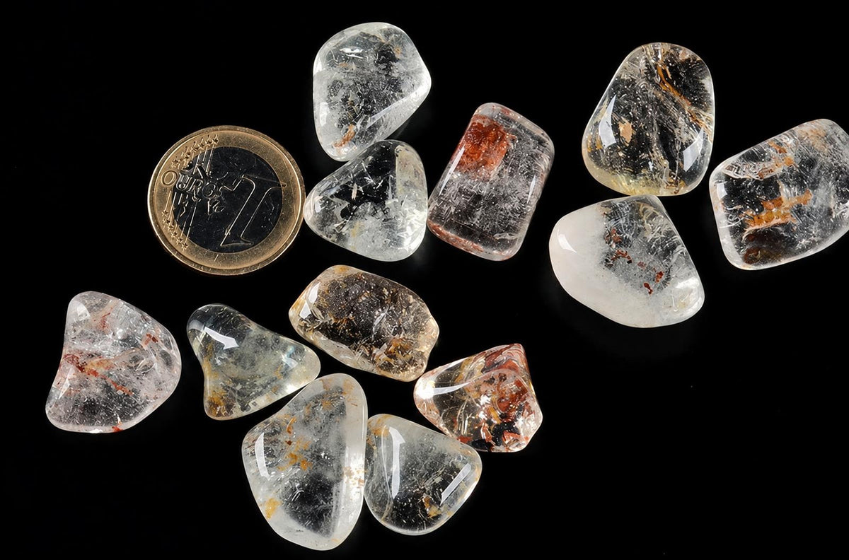 A collection of clear, translucent rough stones with dark and brown inclusions on a black surface next to a two-euro coin.