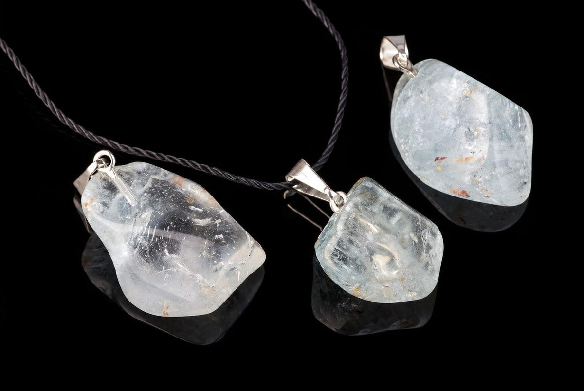 Three silver-toned pendants with pale blue, translucent stones on a dark surface against black background.