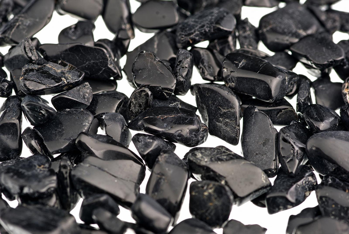 A pile of small, polished black stones with a glossy surface and irregular shapes on a white background.