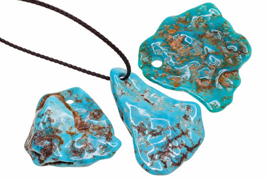 Irregular turquoise pendants display vivid blue colouring with brown veining, including one threaded onto a dark cord against a white background.