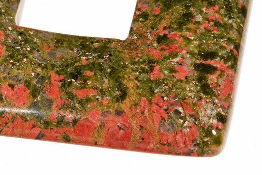 A polished unakite pendant with a square donut shape, featuring red and green speckled patterns on a white background.