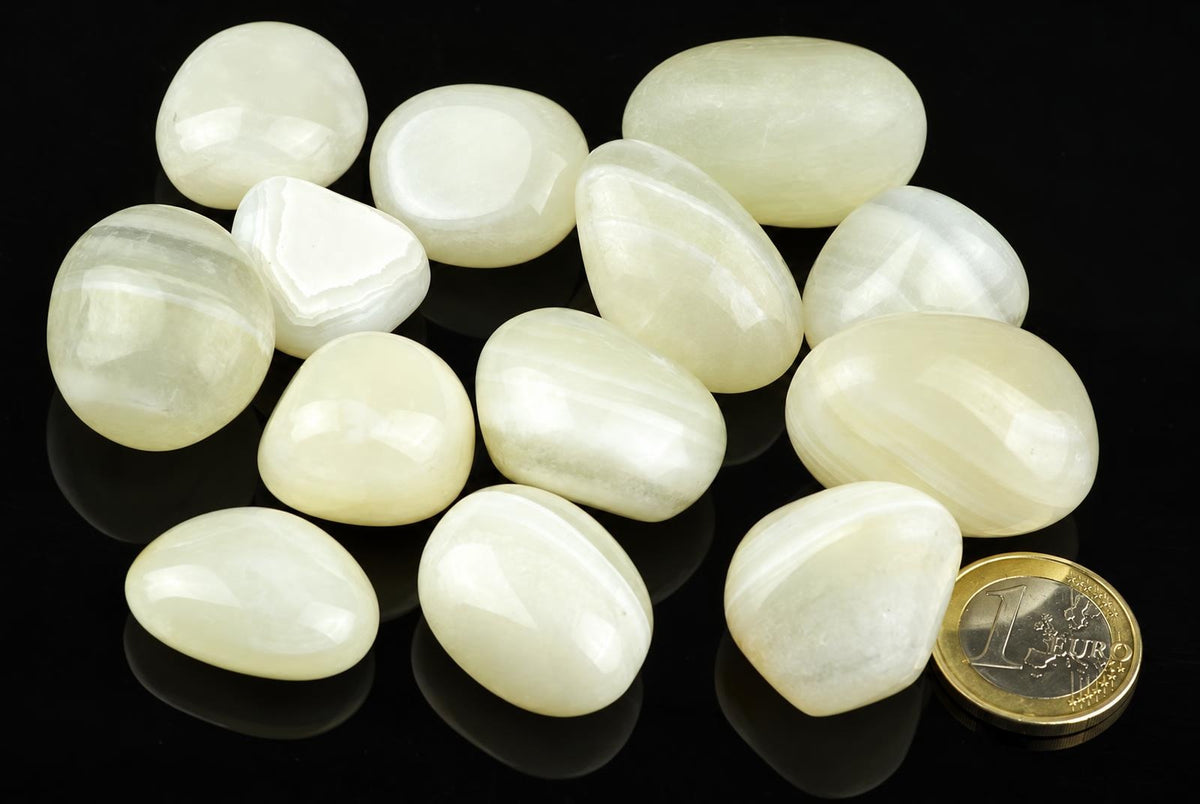 A collection of smooth, polished white and pale yellow stones with subtle banding on a dark surface.