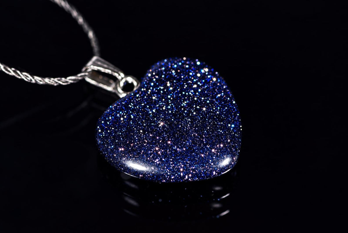 A blue glittery heart-shaped pendant on a silver-tone chain lies on a black reflective surface.