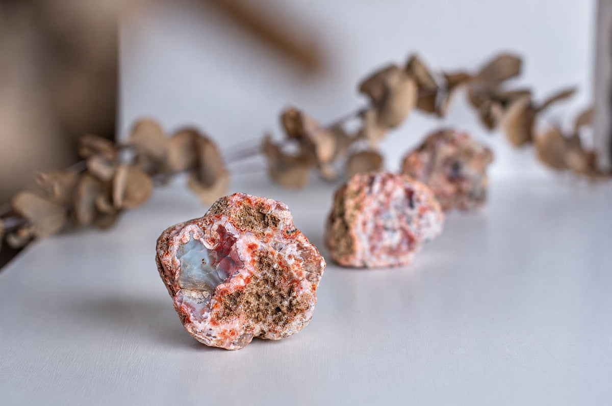 Rough reddish agate stones with grey interiors are arranged in a row on a pale surface.
