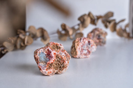 Rough reddish agate stones with grey interiors are arranged in a row on a pale surface.