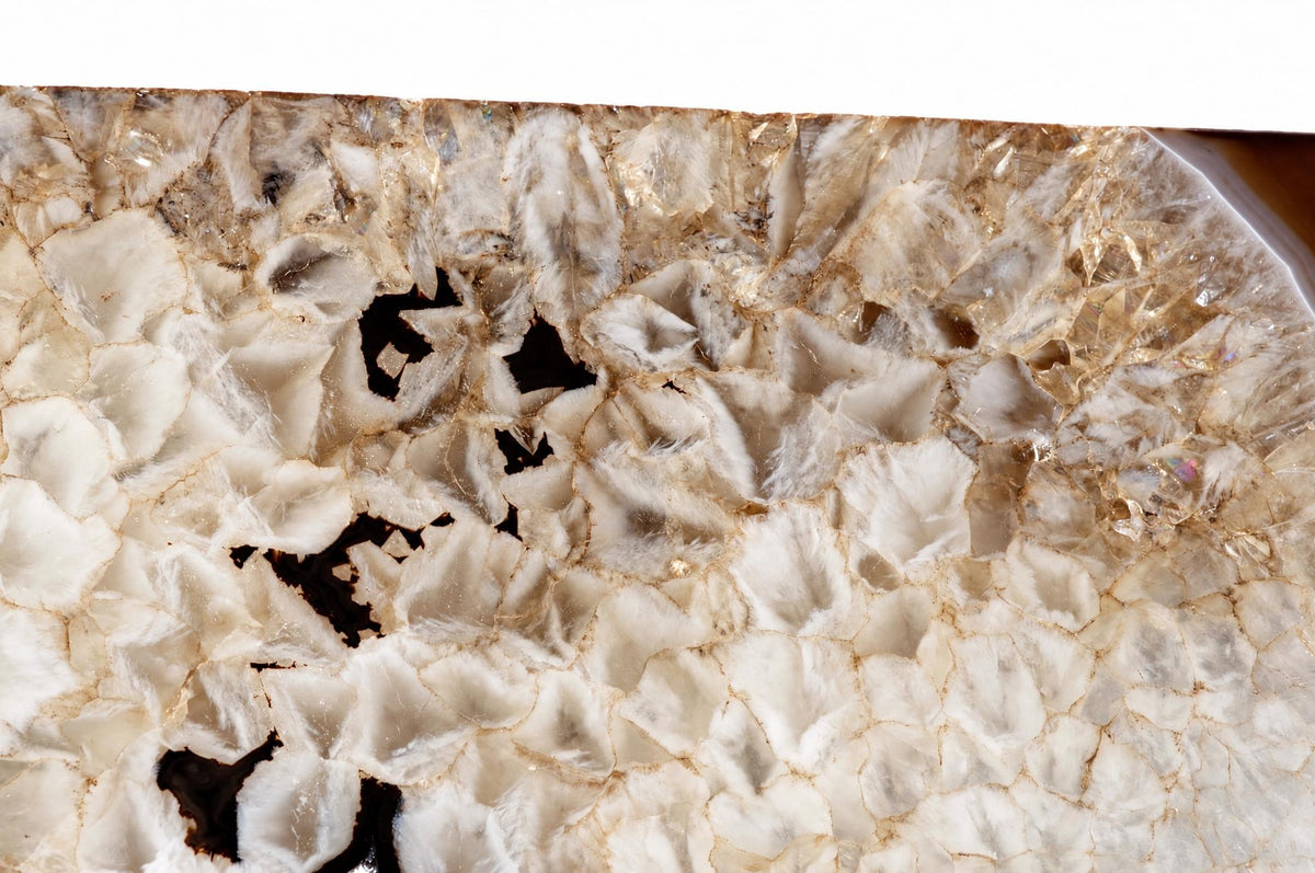 A close-up of a polished agate slice showing white and brown crystalline patterns with dark gaps, resting on a pale surface.