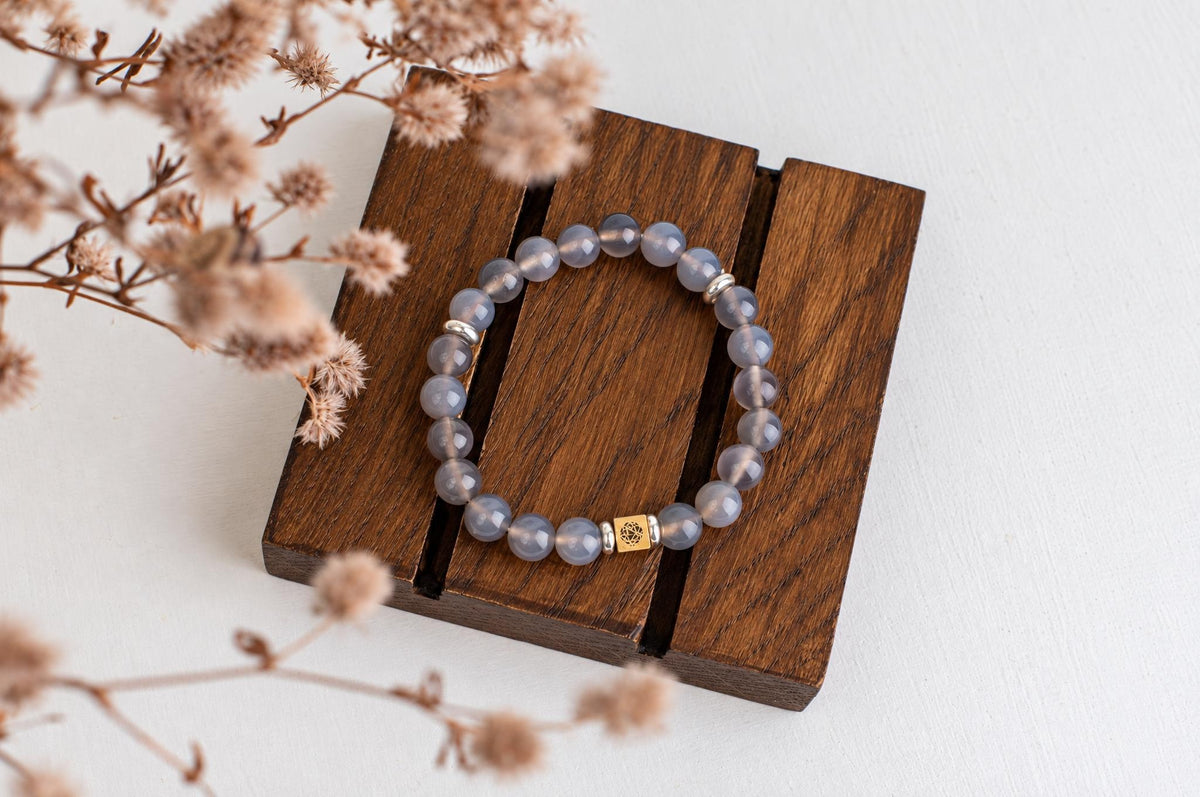 A bracelet with pale blue beads and a gold-toned square charm rests on a dark wooden surface.