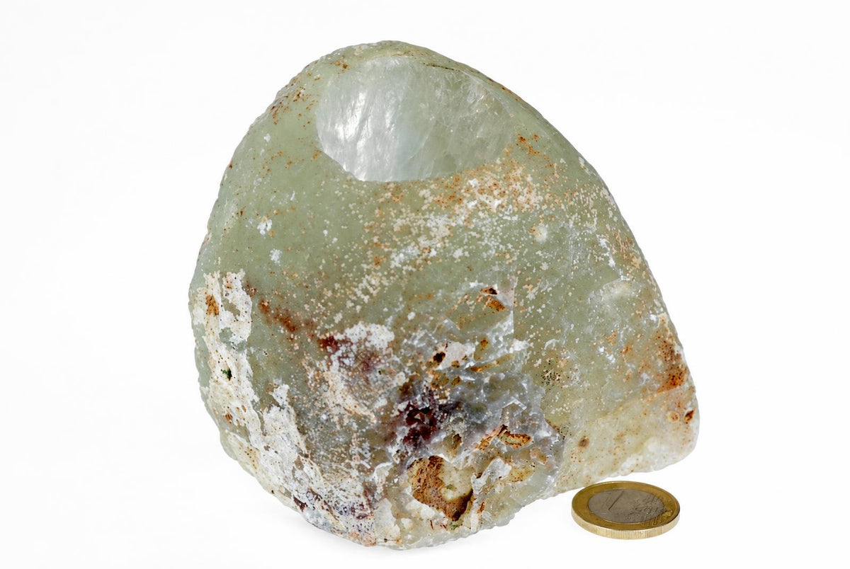 A rough pale agate candle holder with a round hollow stands beside a coin on a white background.