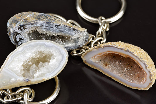 Three polished agate geode slices with silver-toned metal rings and chains on a dark surface.