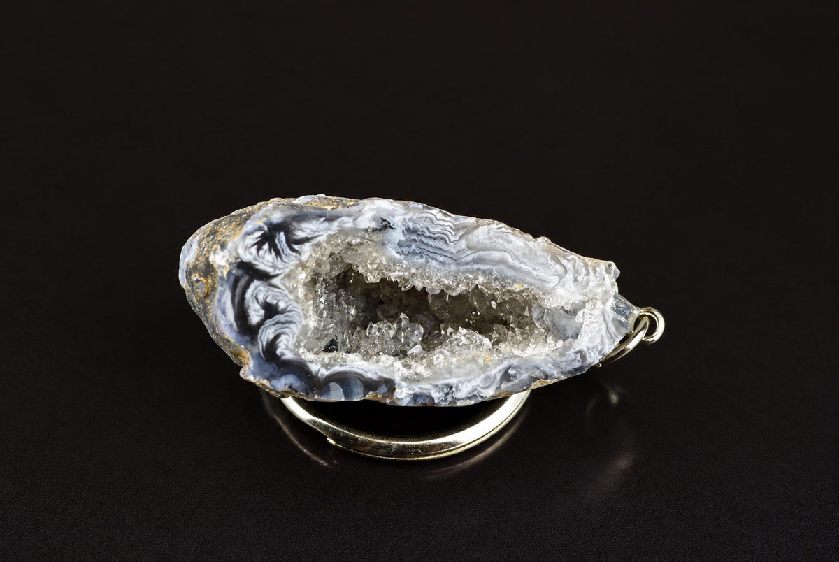 A silver-toned keychain holds a polished agate slice with blue, white and grey swirls on a dark surface.