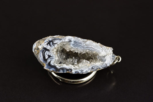 A silver-toned keychain holds a polished agate slice with blue, white and grey swirls on a dark surface.
