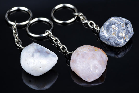 Three polished agate keychains with silver-toned rings and chains rest on a dark, reflective surface.