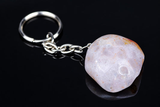 A silver-toned keychain with a polished, pale stone pendant featuring orange-brown spots and circular indentations on a dark reflective surface.