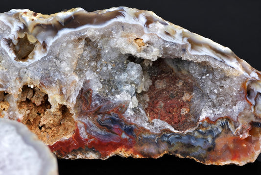 A cut agate nodule shows grey banding and crystal cavities in a rough red and brown outer crust.