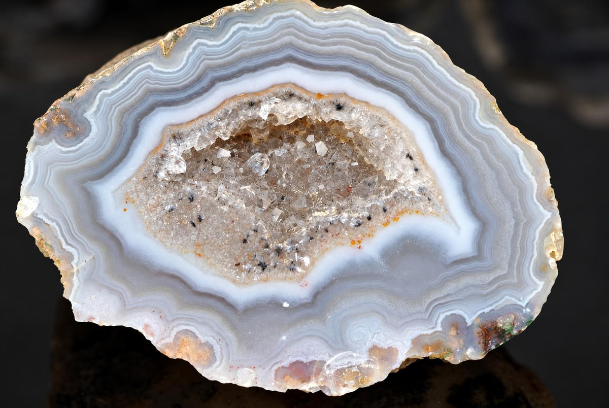 A round agate slice shows concentric pale grey bands surrounding a sparkling crystal centre.