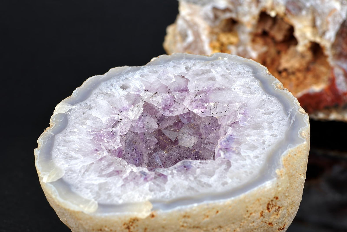 An open agate nodule shows a pale purple crystal cavity surrounded by white and grey bands.
