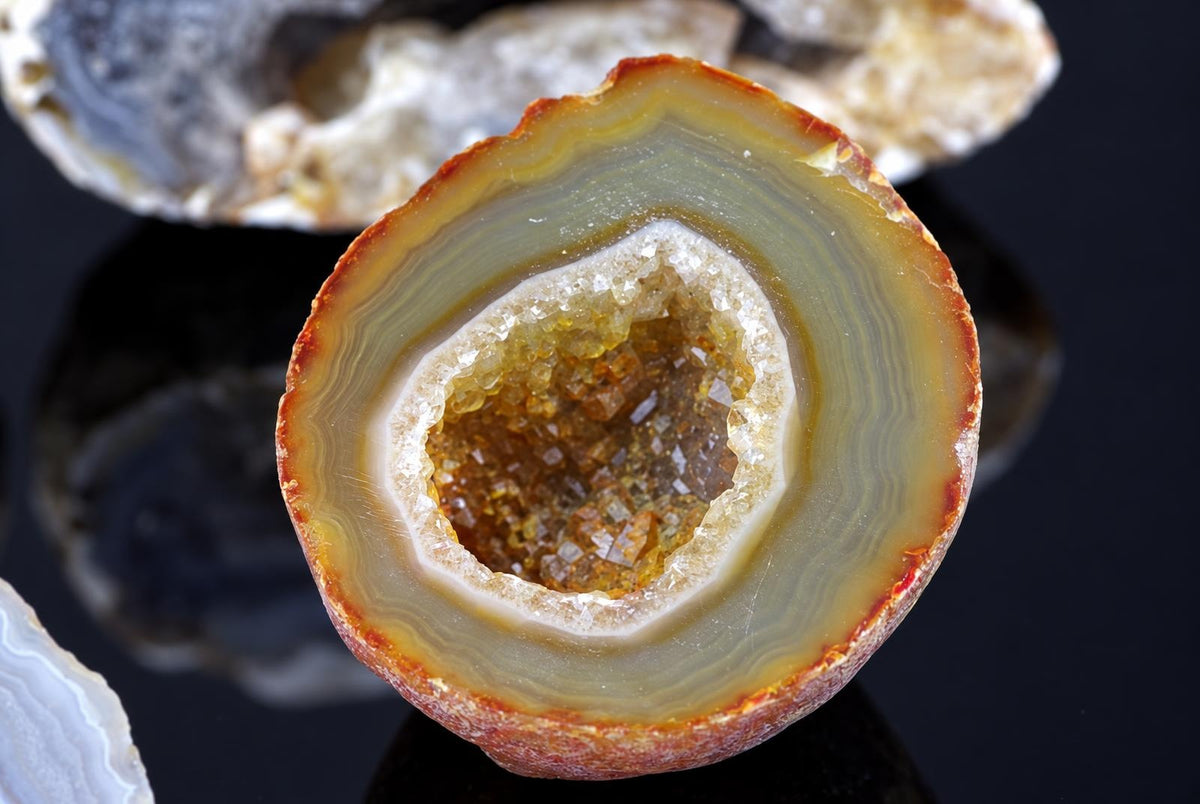 A sliced agate geode with concentric bands of brown, tan and white, revealing a central cavity lined with yellowish crystals on a dark surface.