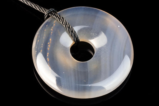 A translucent, donut-shaped pendant with a central hole and subtle internal banding, suspended by a twisted cord against a dark surface.
