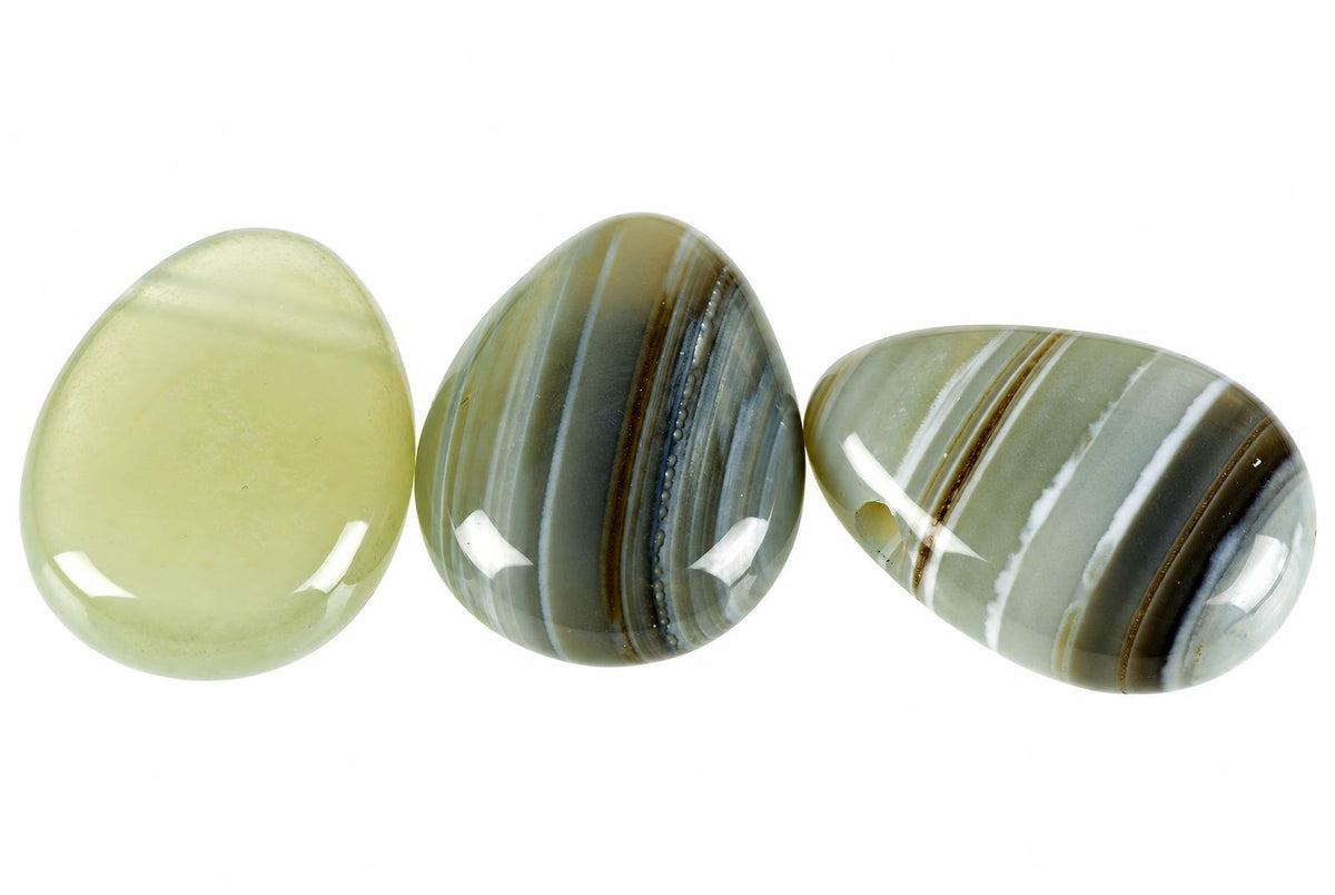 Three polished agate stones on a white background. The left stone is pale yellow-green, while the other two display striped patterns in grey, brown and white.