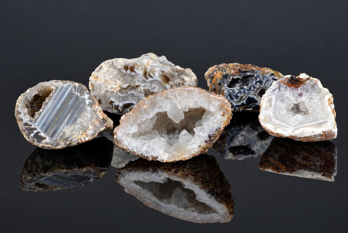 Five polished agate geodes with crystalline interiors in white, grey and dark bands on a dark reflective surface.