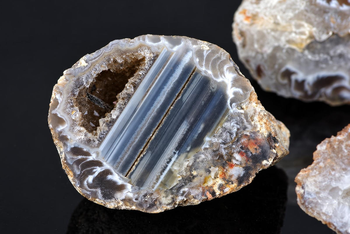 A polished agate slice with a dark surface, showing white and grey banding inside on a black background.