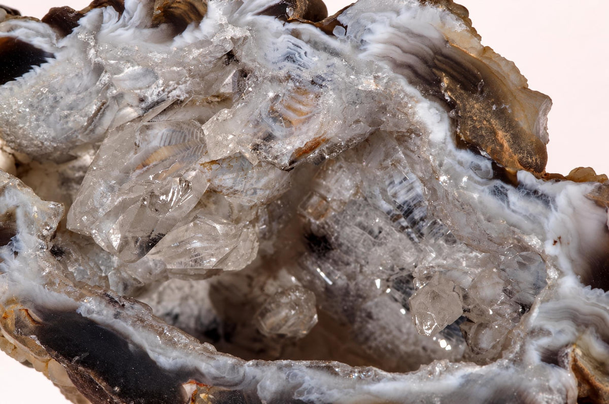 A close view of raw agate shows translucent crystals within an uneven hollow, bordered by layered grey, white and brown surfaces.