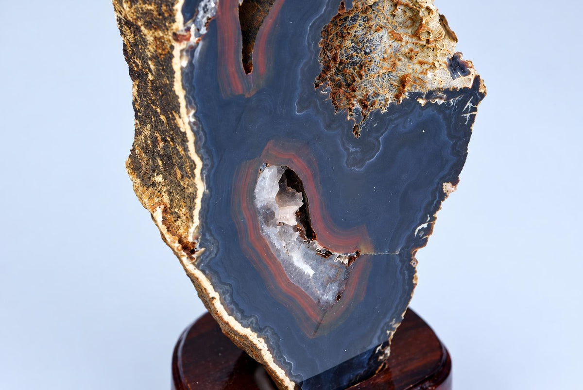 A polished agate slice with dark blue, red and white bands sits on a wooden base against a pale background.