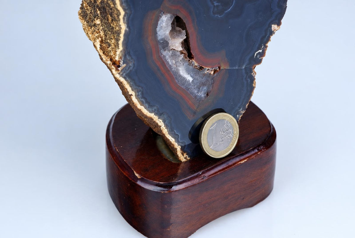 A polished agate slice with dark blue, red and white bands on a wooden base, next to a one euro coin.
