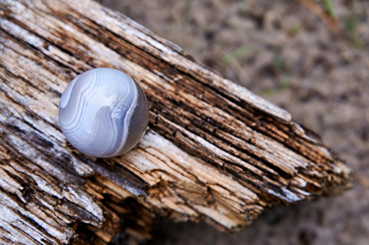 A polished agate sphere with white and grey swirls rests on a weathered wooden surface.