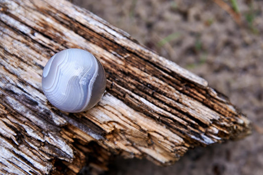 A polished agate sphere with white and grey swirls rests on a weathered wooden surface.