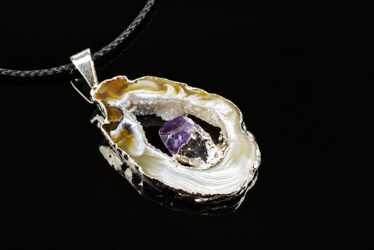 A silver-toned pendant with a polished agate slice showing white, cream and brown swirls, containing a purple amethyst crystal on a dark surface.