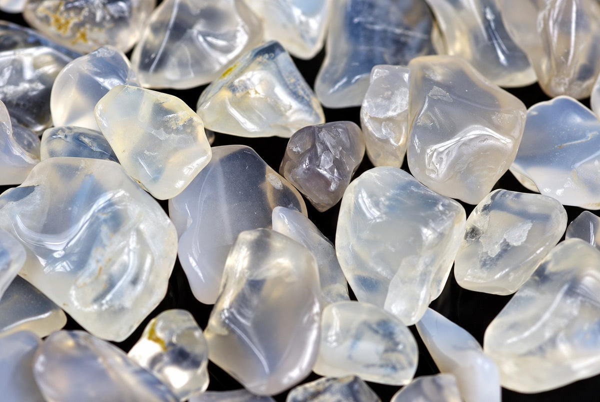 A pile of small, polished agate stones in white and blue tones on a dark surface.