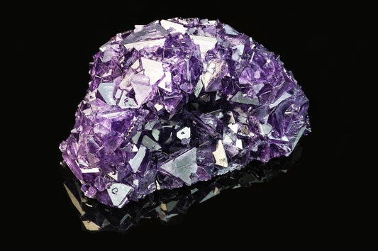 A cluster of purple and clear alum crystals on a dark, reflective surface.