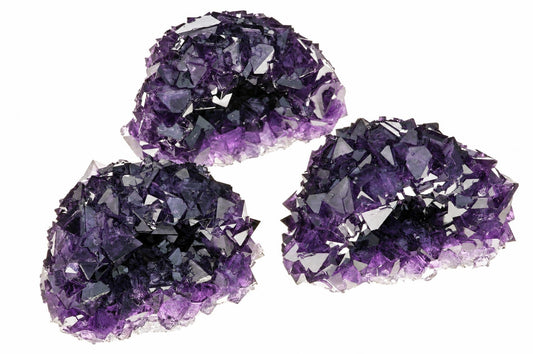 Three purple alum crystals with jagged, reflective surfaces arranged on a white background.