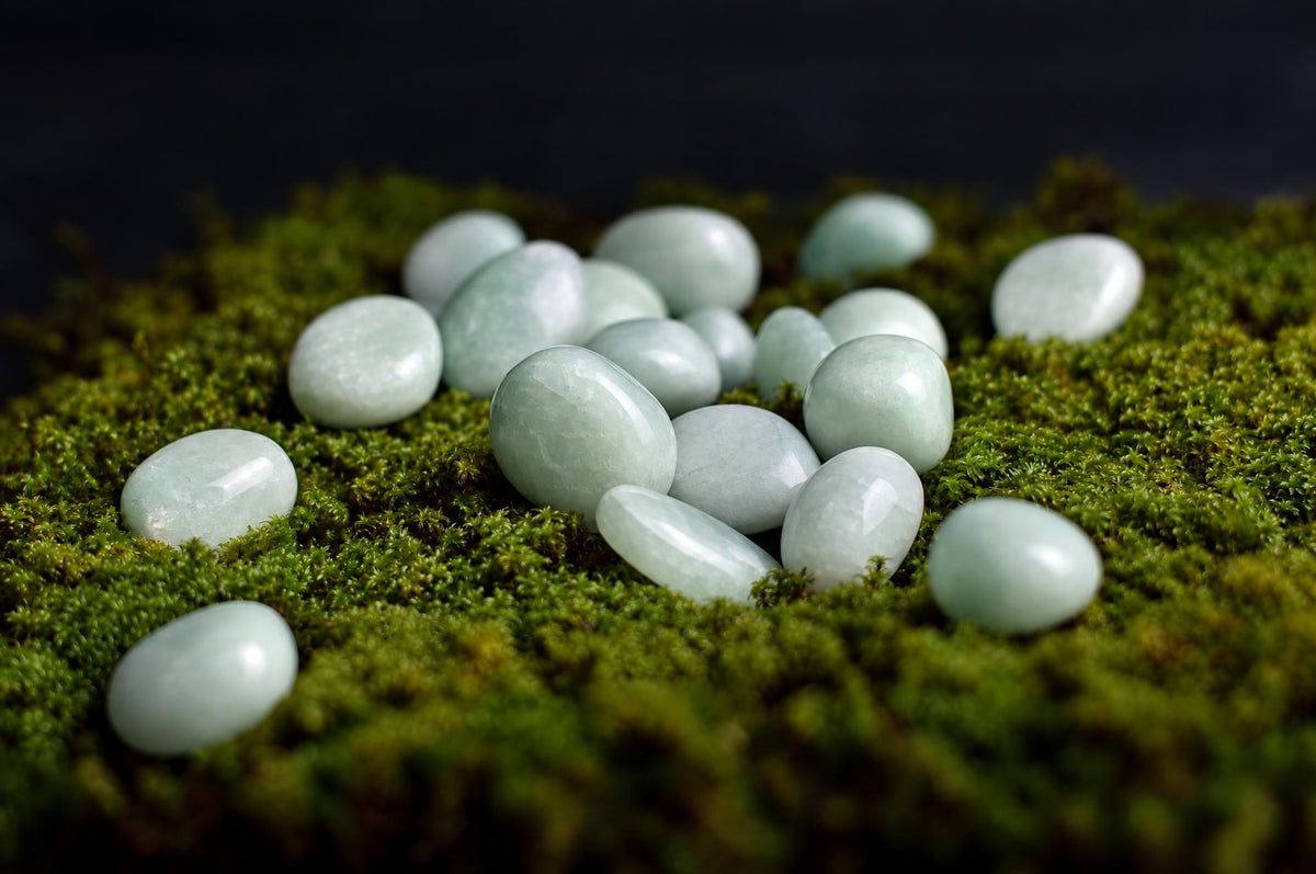 Several smooth, pale green Amazonite stones rest on a dark green mossy surface against a black background.