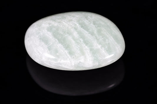 A polished, oval-shaped stone with a pale green and white swirled pattern rests on a dark surface.