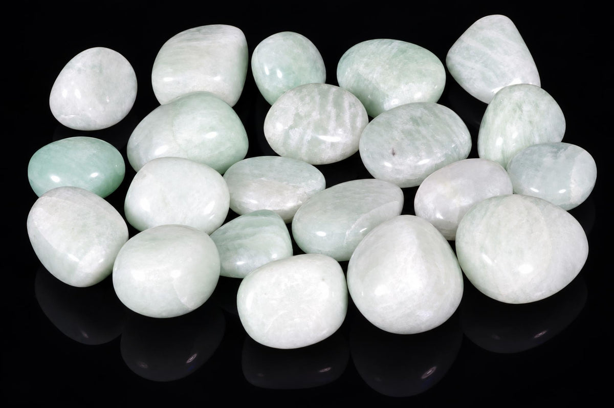 A collection of smooth, polished Amazonite stones in pale green and white tones arranged on a dark reflective surface.