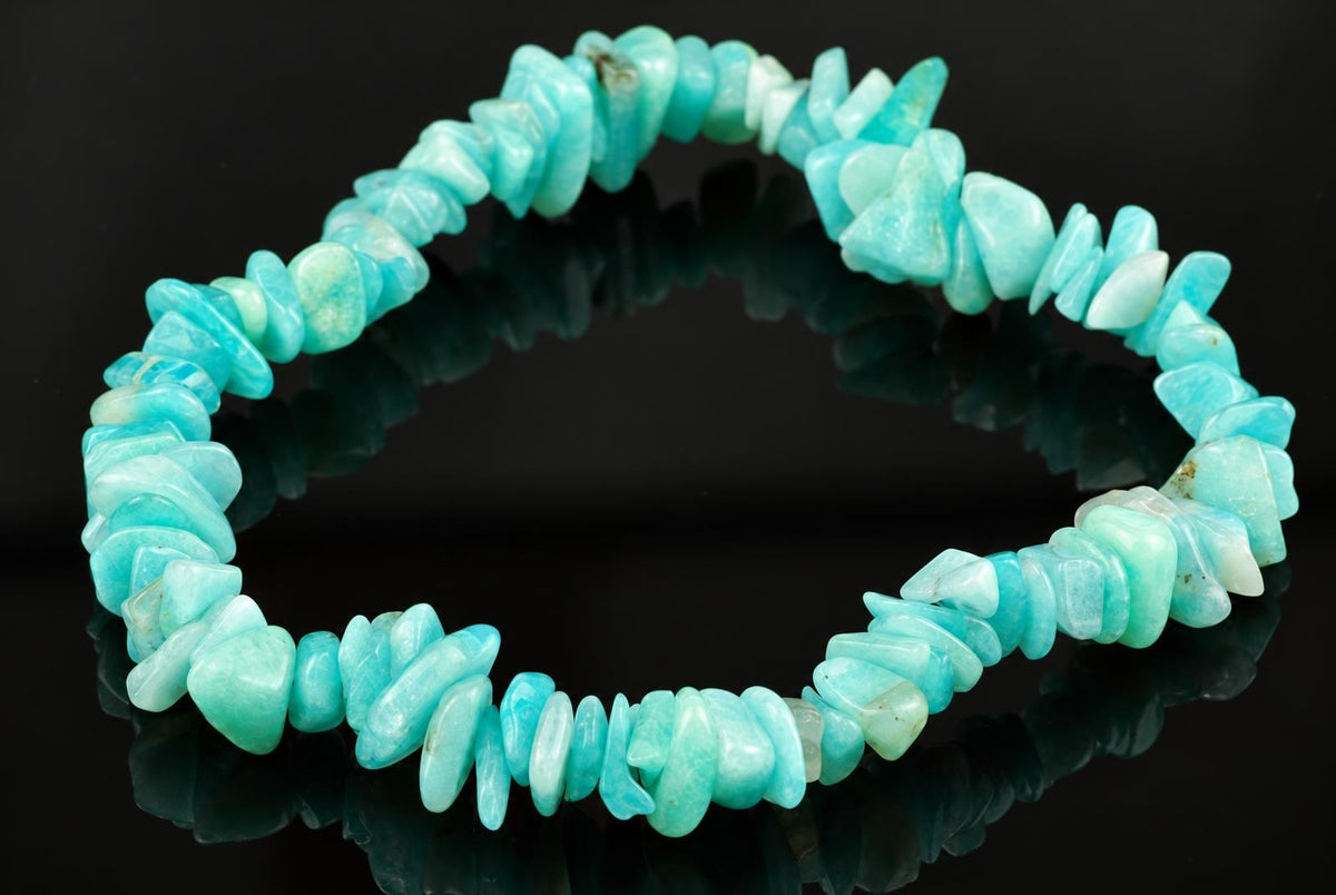 A bracelet made of irregular, polished chips of light blue to pale green amazonite stones arranged in a circle on a dark reflective surface.