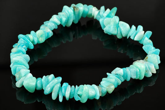 A bracelet made of irregular, polished chips of light blue to pale green amazonite stones arranged in a circle on a dark reflective surface.