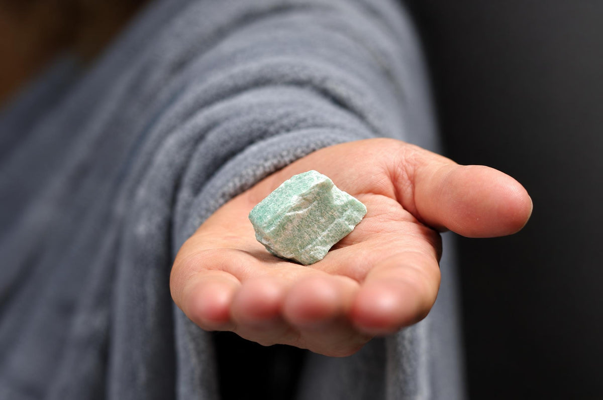A hand holds a rough, light green and white mineral specimen against a dark background.