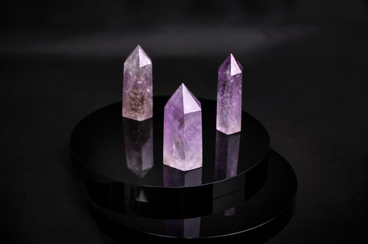 Three purple amethyst crystal points stand on a dark, reflective circular surface against a black background.